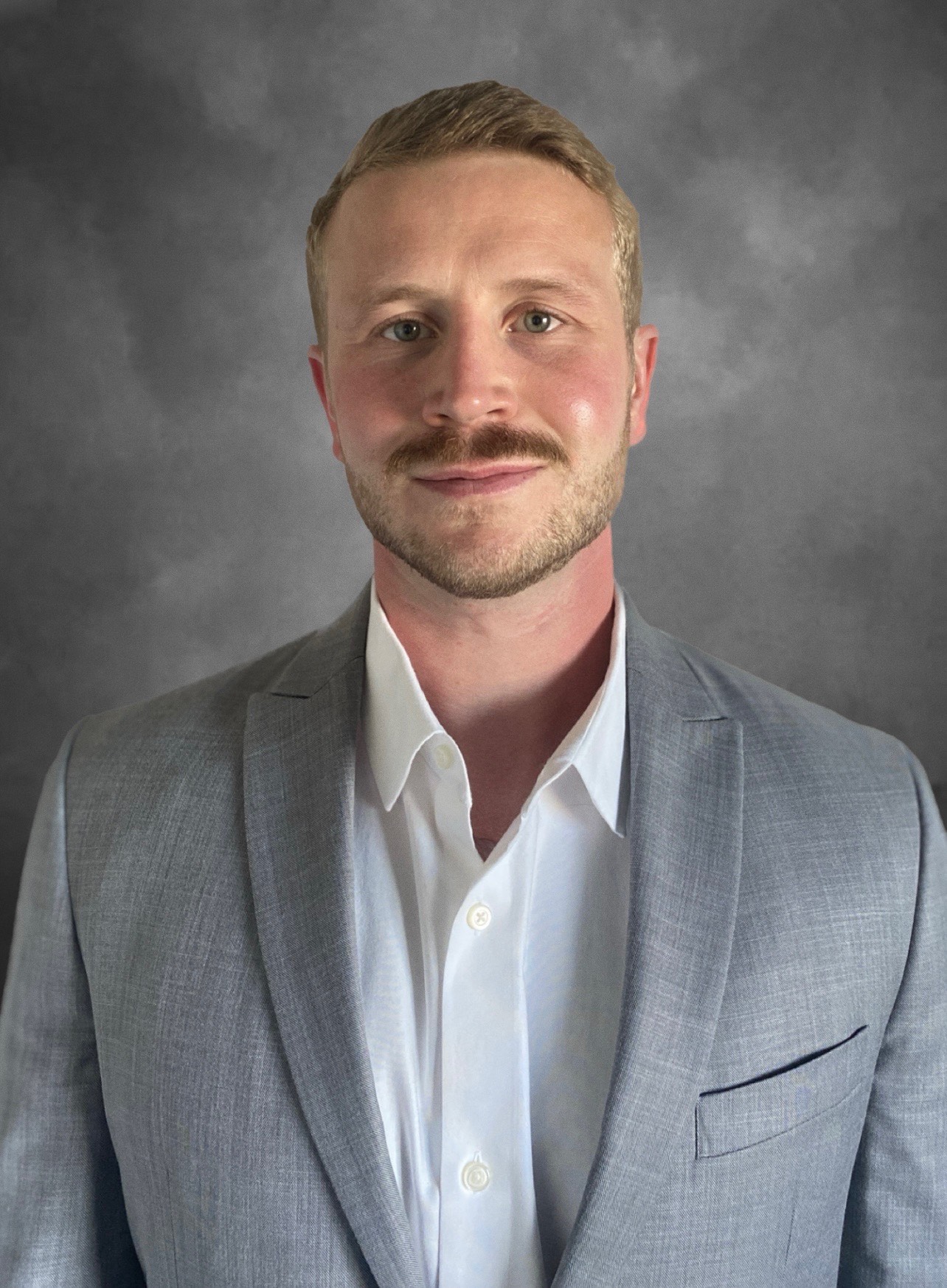 Professional headshot of a man in gray blazer and white shirt against neutral background