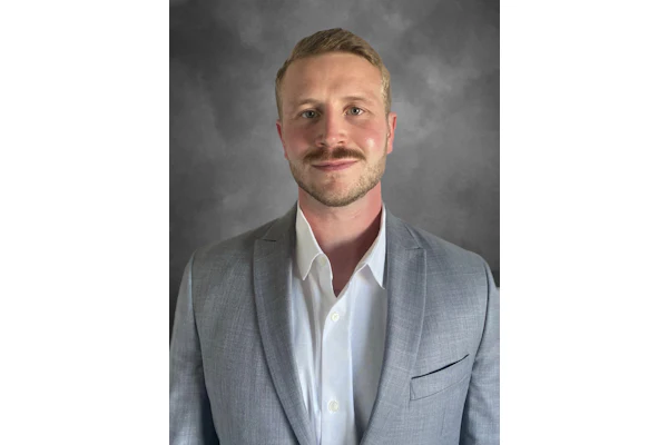 Professional headshot of a man in gray blazer and white shirt against neutral background