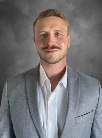 Professional headshot of a man in gray blazer and white shirt against neutral background