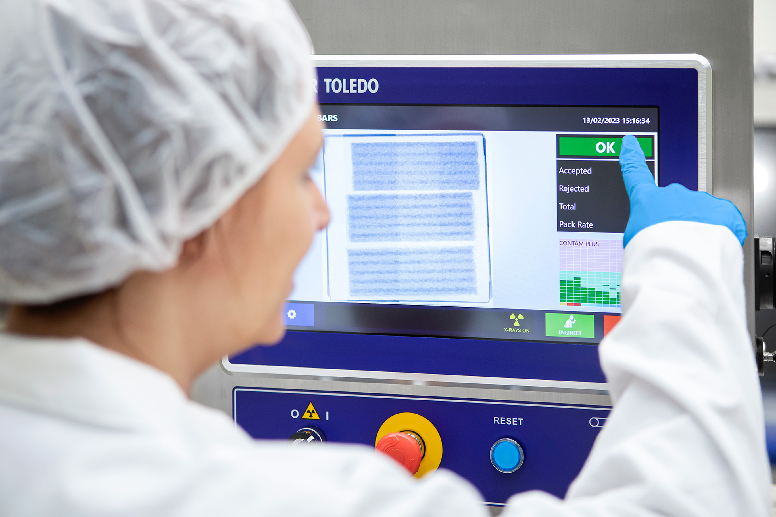 Operator in cleanroom suit using TOLEDO quality control inspection device displaying scan results and acceptance metrics