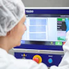 Operator in cleanroom suit using TOLEDO quality control inspection device displaying scan results and acceptance metrics