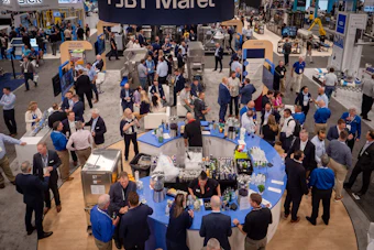 Overhead view of crowded trade show floor with blue booth tables, attendees in business attire, and exhibition signage
