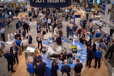 Overhead view of crowded trade show floor with blue booth tables, attendees in business attire, and exhibition signage