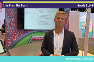 Professional man in blazer presenting at Pack Expo booth with display screen and red patterned backdrop
