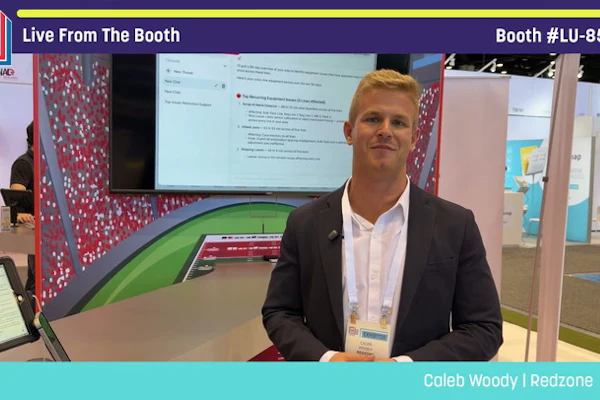 Professional man in blazer presenting at Pack Expo booth with display screen and red patterned backdrop