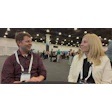 Two professionals wearing conference badges engage in conversation at an indoor event venue.