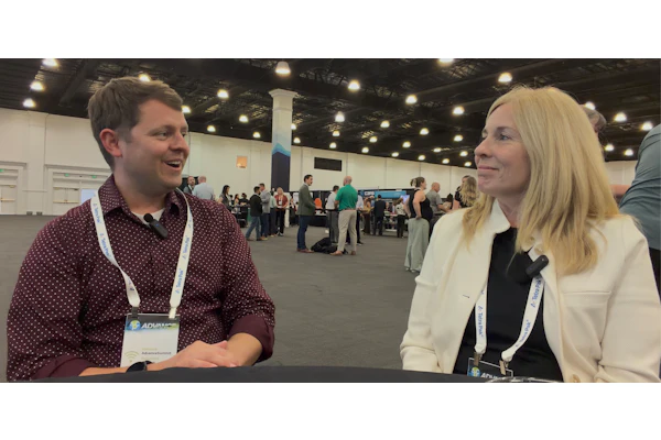 Two professionals wearing conference badges engage in conversation at an indoor event venue.