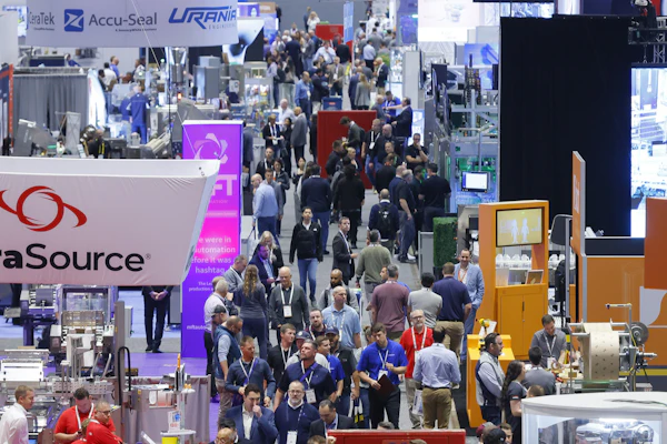 Busy trade show exhibition floor with multiple vendor booths, attendees in business attire, and corporate signage including DataSource, Accu-Seal, and Urani branding.