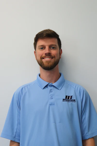 Professional headshot of smiling man with beard wearing light blue Morrison company polo shirt against neutral background