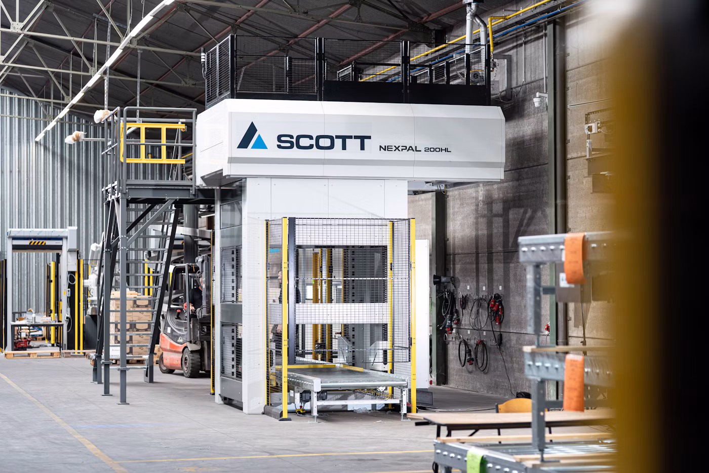 Scott Technology's Nexpal industrial hydraulic press machine in factory warehouse with yellow safety railings and equipment