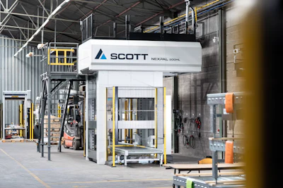 Scott Technology's Nexpal industrial hydraulic press machine in factory warehouse with yellow safety railings and equipment