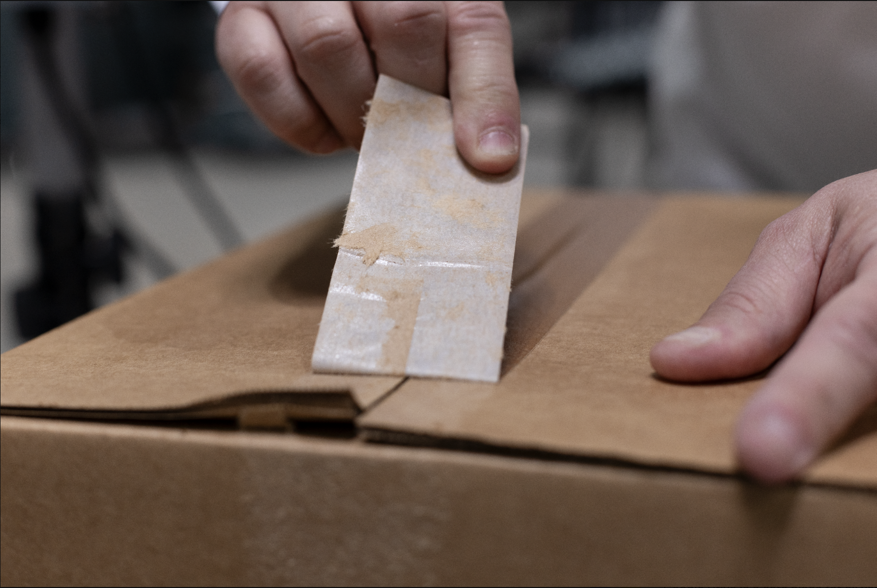 Person sealing a cardboard box with clear tape during packaging