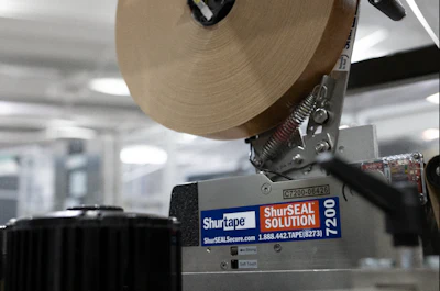Shurtape ShurSEAL SOLUTION tape dispenser with tan-colored tape roll mounted on industrial packaging machine