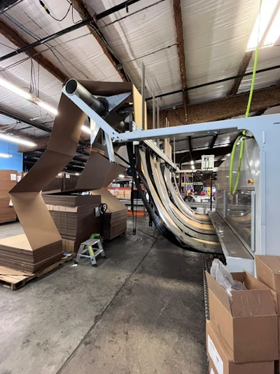 Fanfold corrugated feeds the EM7-35 from pallets beside the machine. SMA runs single- and double-wall corrugated in three fanfold widths.